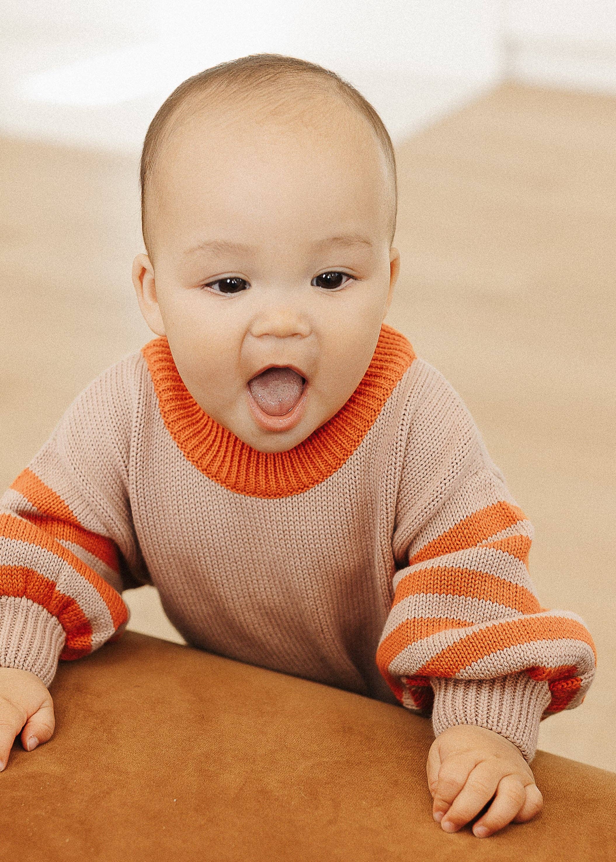 Baby in a striped outfit sitting on a brown surface with a white background