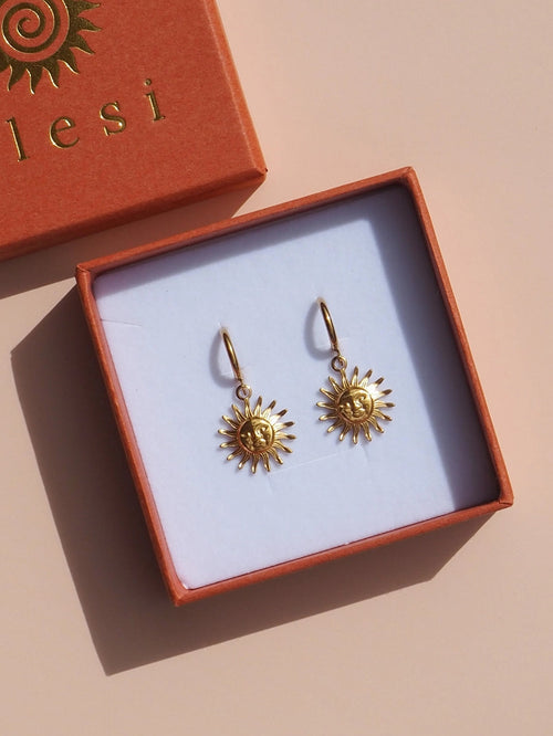 Gold sun-shaped earrings in a 'calesi' branded box on a beige background