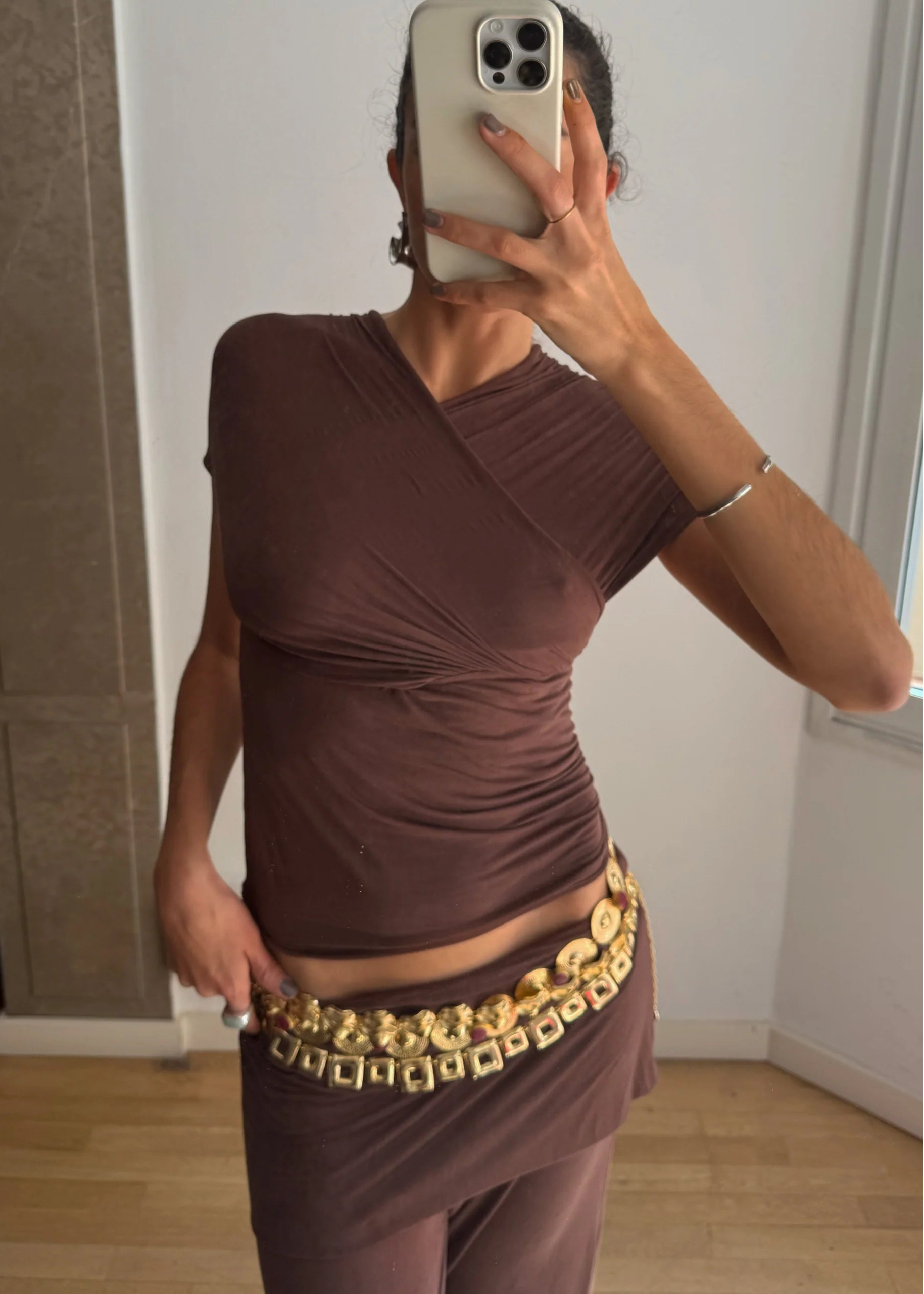 Person wearing a brown top and gold belt taking a mirror selfie.