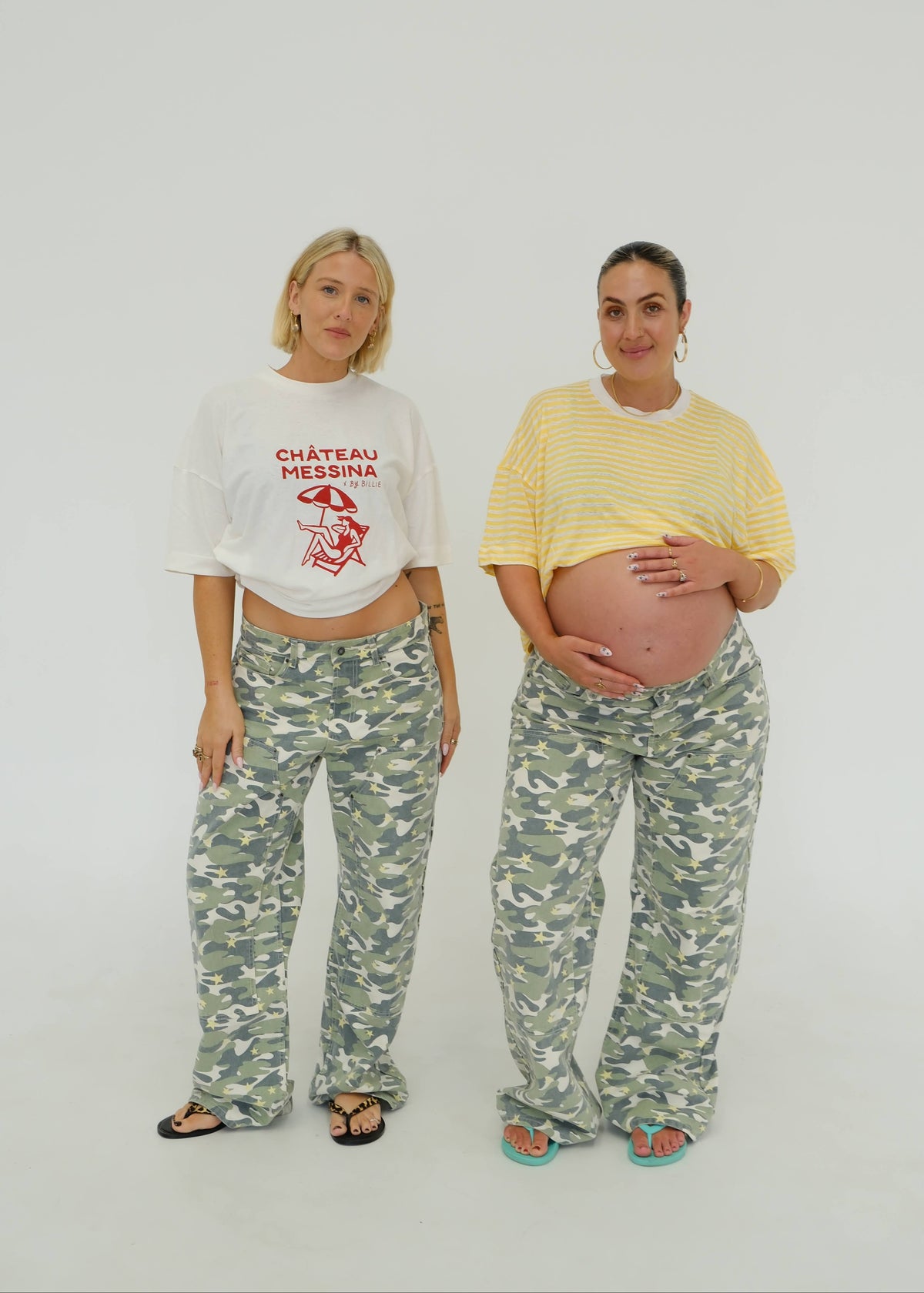 Two women standing against a plain light gray studio background. The woman on the left wears a white cropped T-shirt with red 'CHÂTEAU MESSINA' text and a red graphic, paired with green-gray camouflage pants.