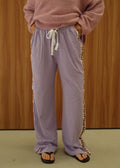 A person wearing a dusty pink fuzzy knit sweater and lavender wide-leg sweatpants with a white drawstring and striped side detailing, standing against a wood-paneled wall.