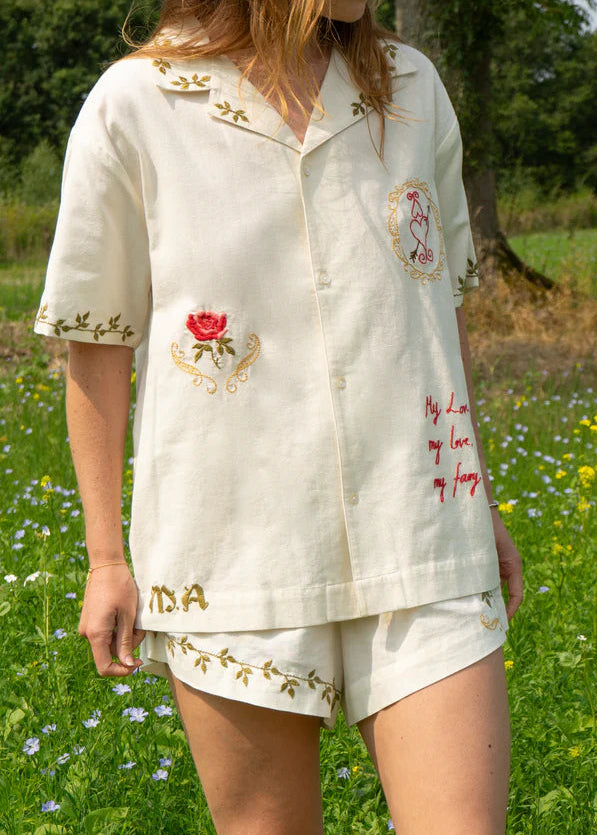 Person wearing a white embroidered outfit in a natural setting with greenery and flowers.