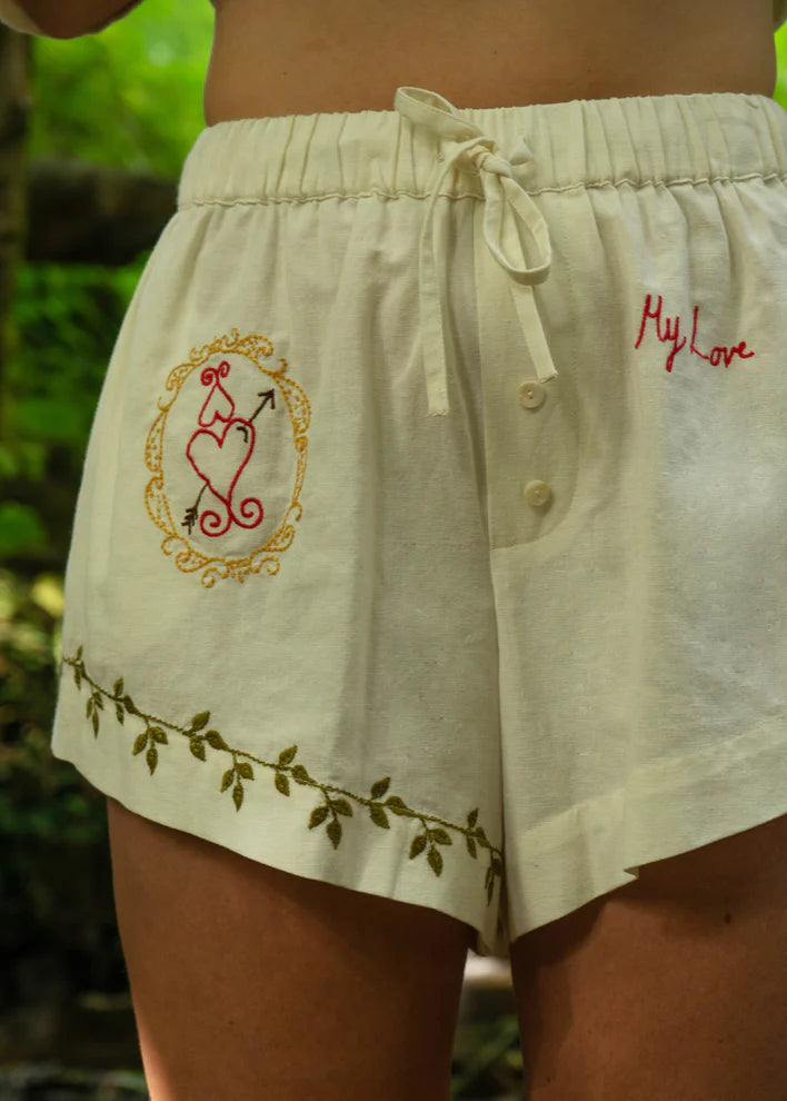 Beige shorts with embroidery and text against a blurred green background