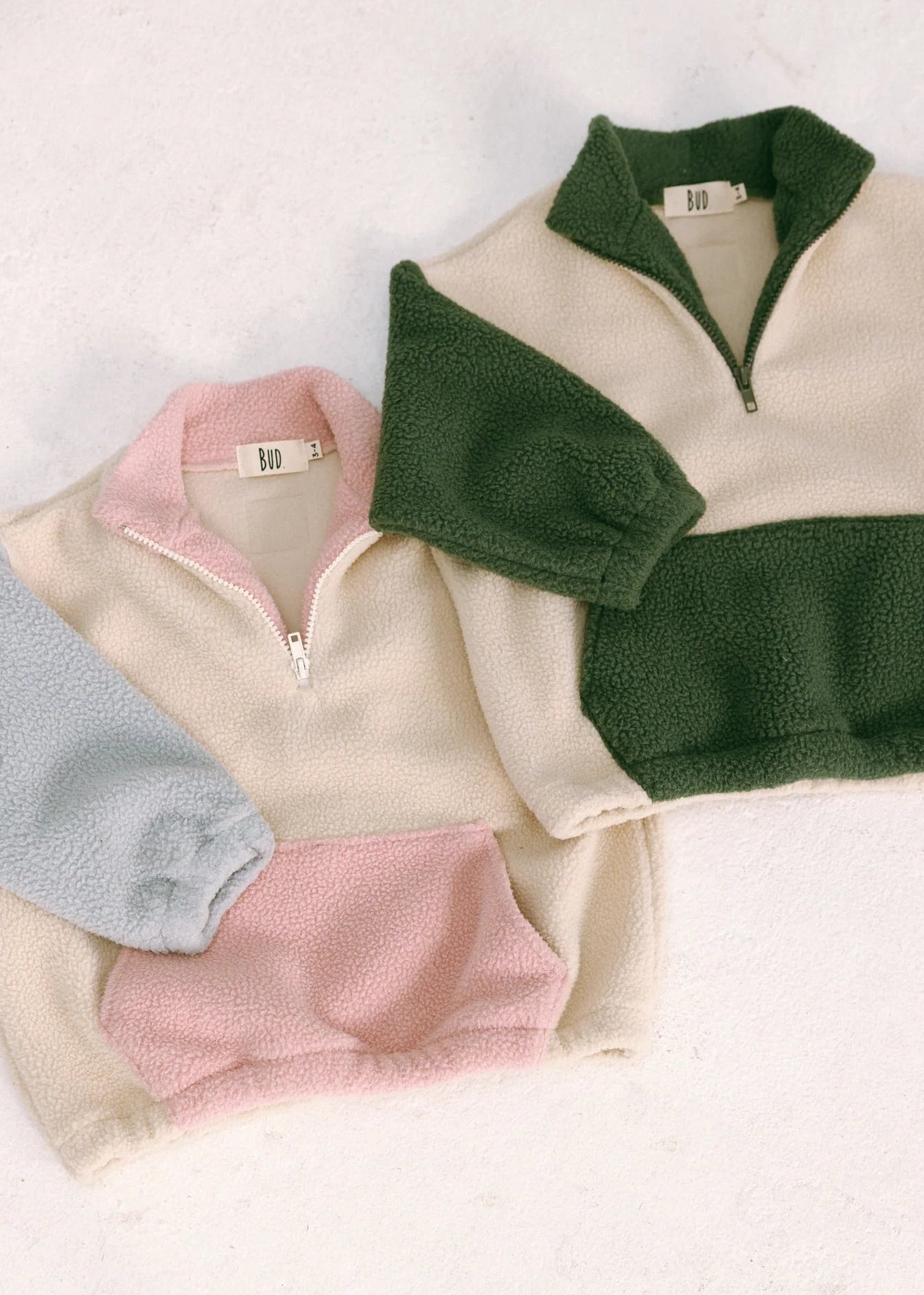 Three fleece pullovers in green, pink, and gray on a light background