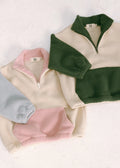 Three fleece pullovers in green, pink, and gray on a light background