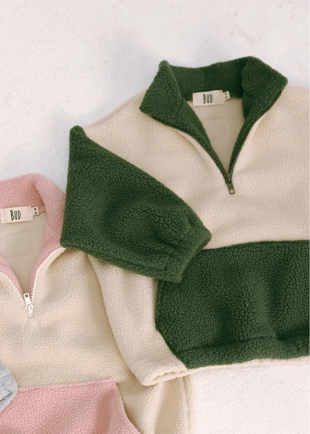 Three fleece pullovers in green, pink, and gray on a light background