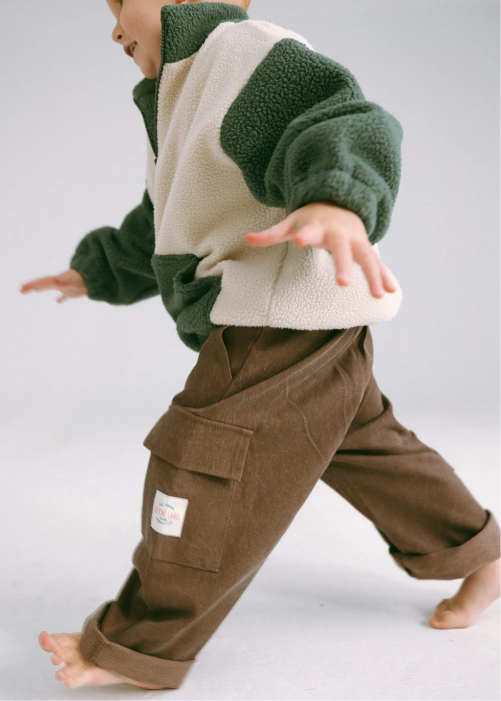 Child wearing a green and beige sweater with brown pants on a white background