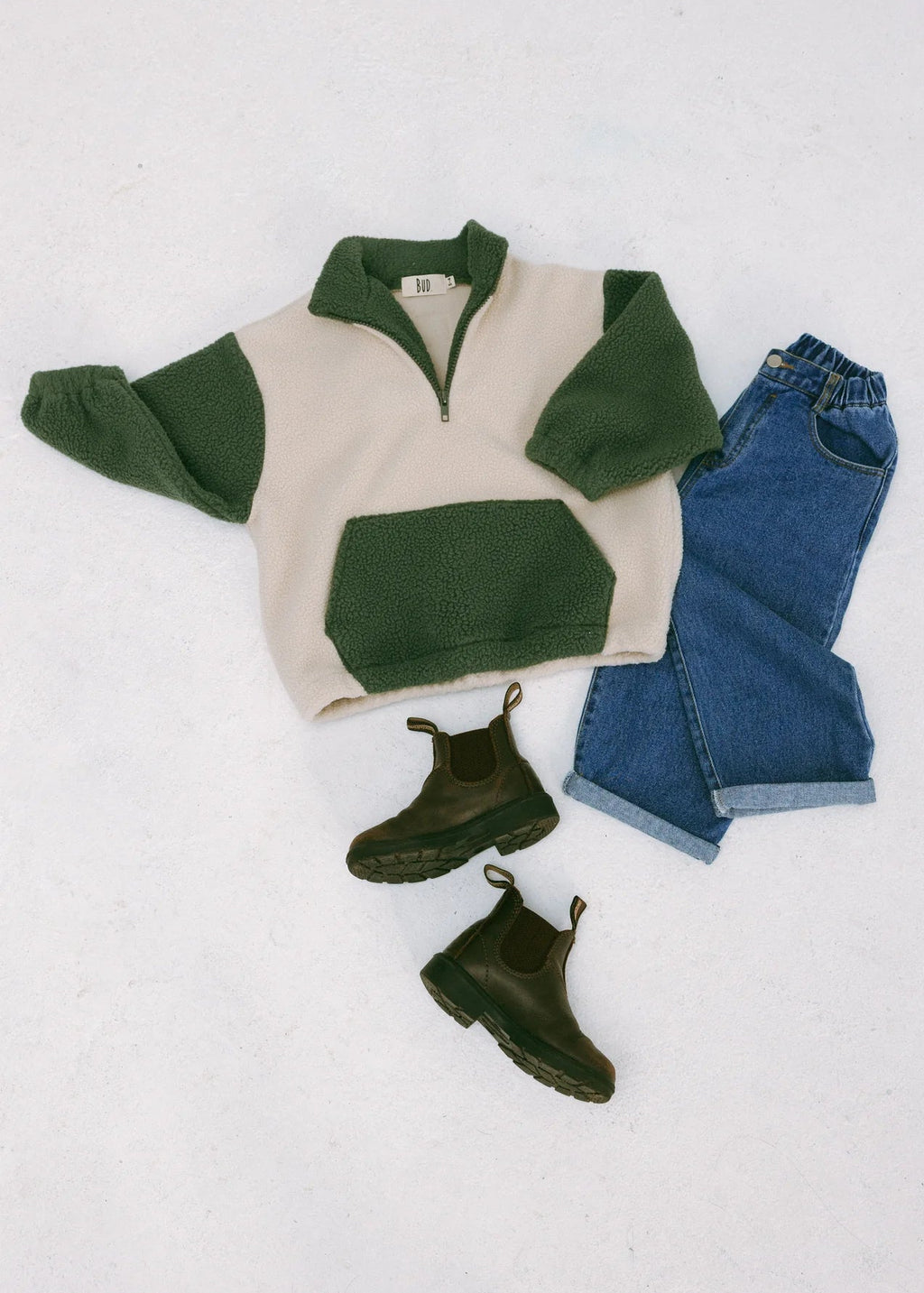 Green and beige sweater, blue jeans, and green boots on a white background