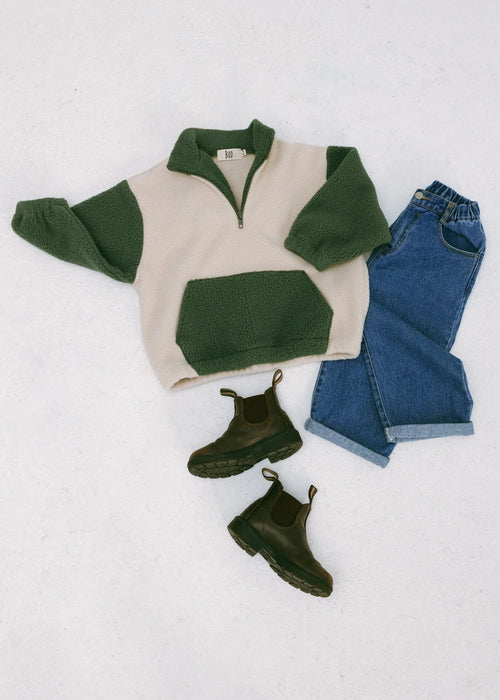 Green and beige sweater, blue jeans, and green boots on a white background