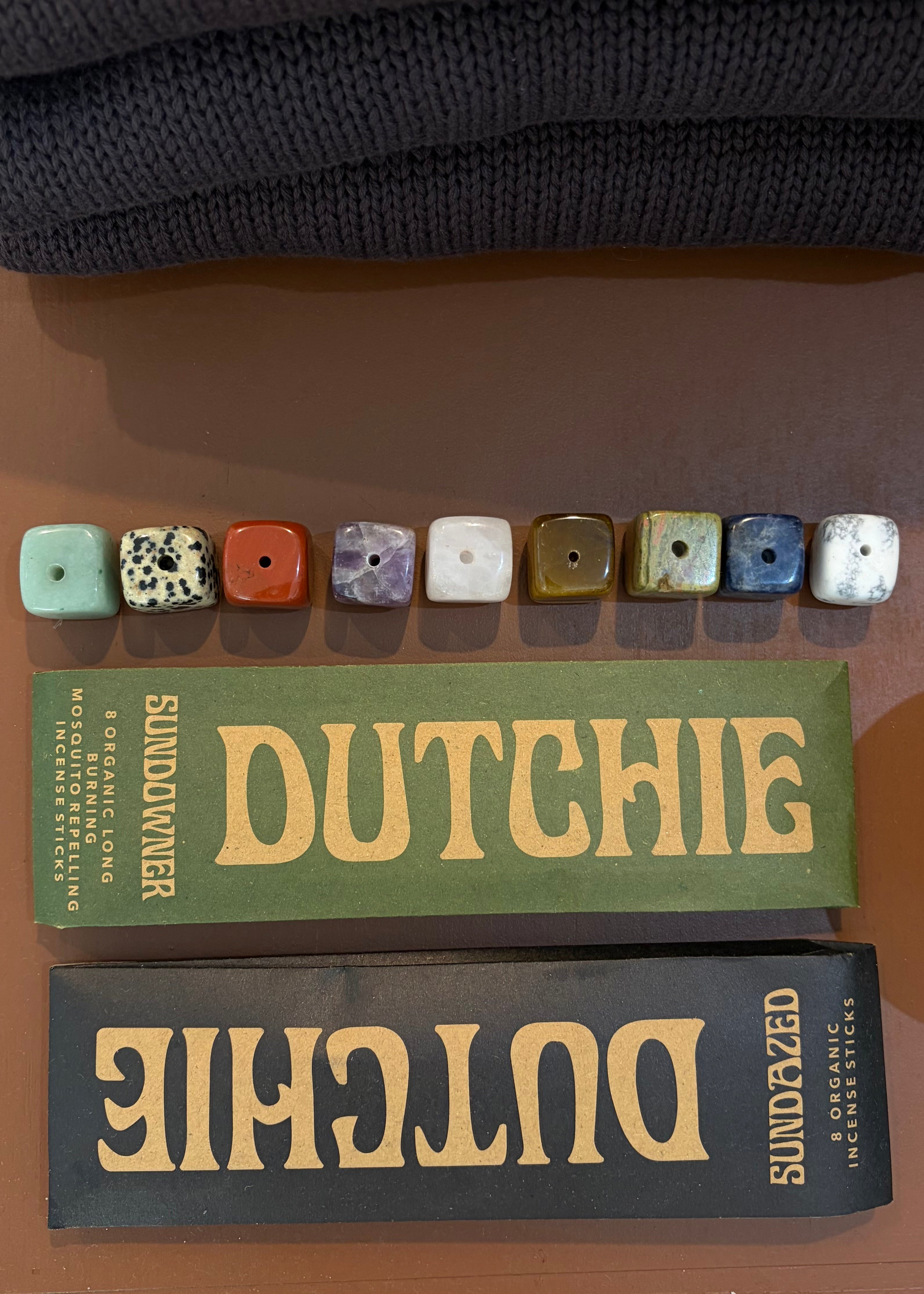 A set of nine square stone beads in various colors and patterns, displayed above two vintage-style book covers featuring the title 'DUTCHIE' and the brand 'SUNDAZED'.