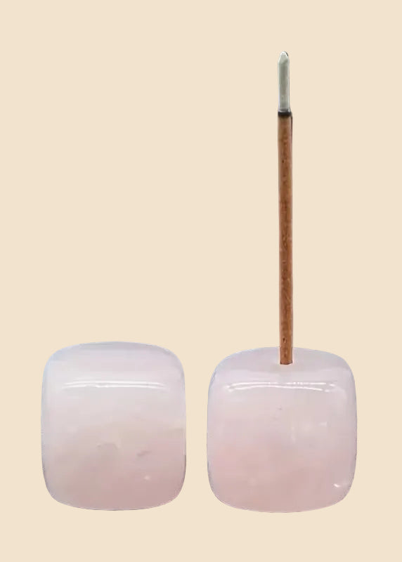 Two pale pink stone incense holders on a light beige background, with one holder containing a single incense stick.