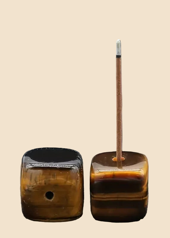 Two amber-brown glass incense holders on a solid beige background, one closed and one open with a single incense stick inserted.