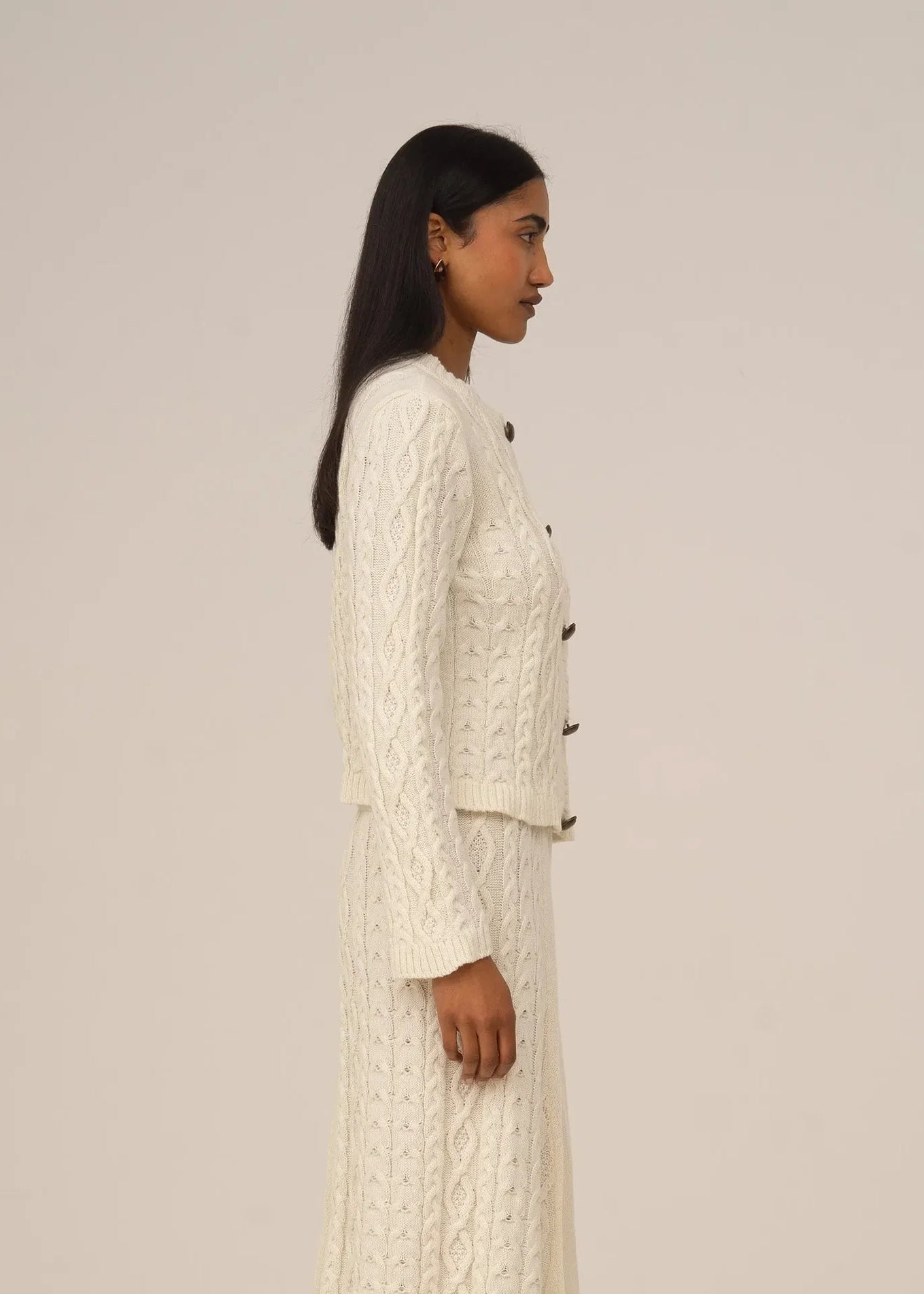 Woman wearing a white cable knit outfit against a plain background