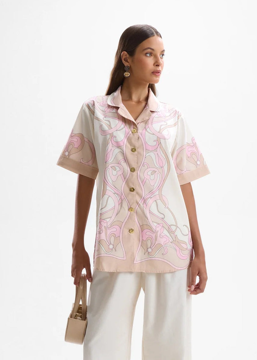 Woman wearing a light pink and white outfit with a patterned top and white pants on a white background