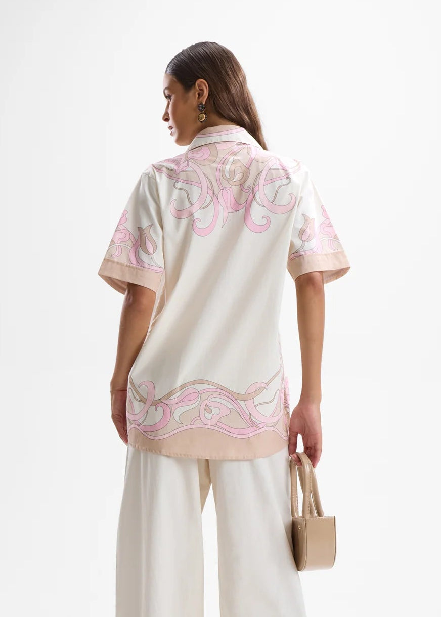 Woman wearing a cream outfit with pink patterns on a white background
