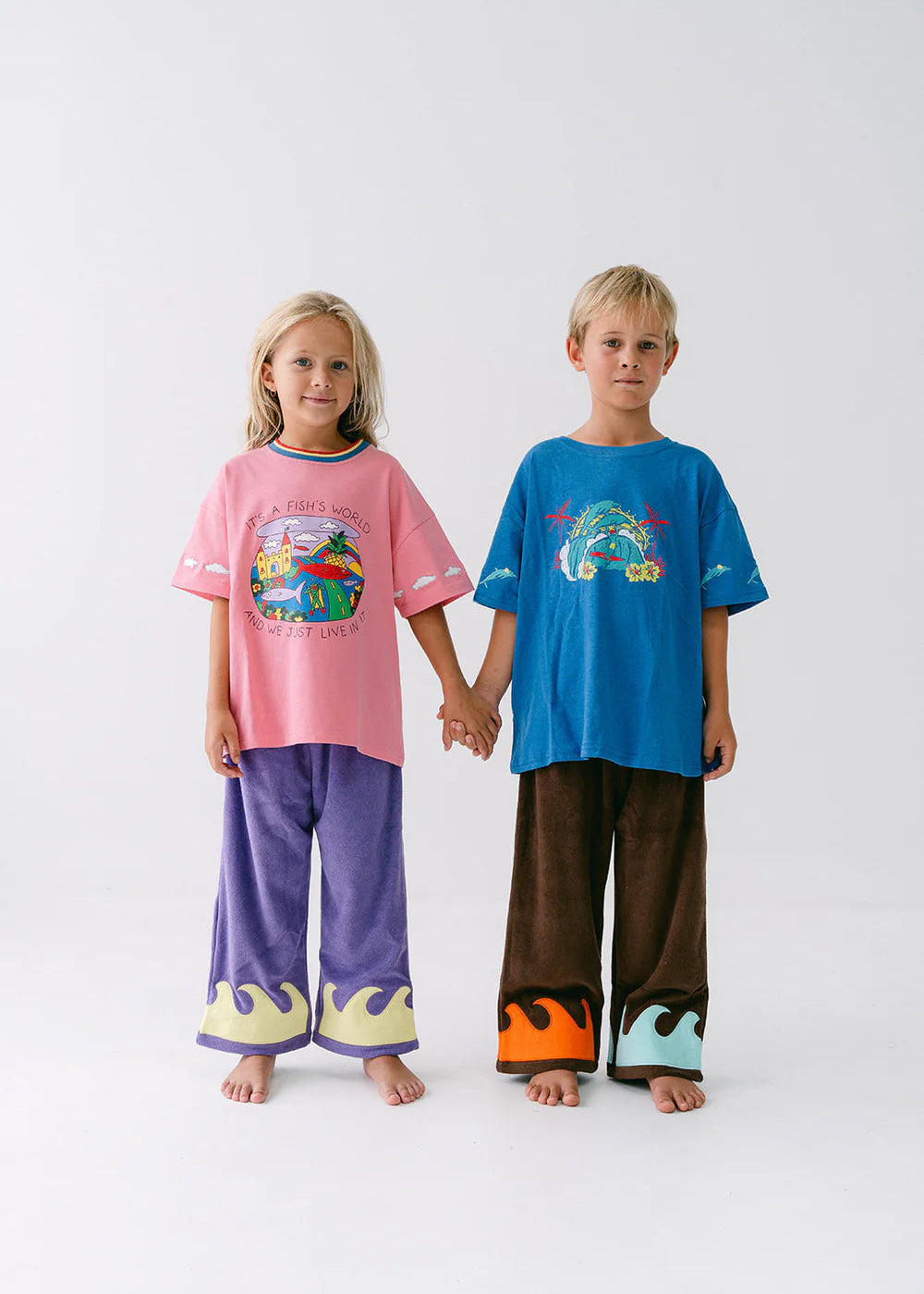 Two children wearing colorful pajamas holding hands on a white background
