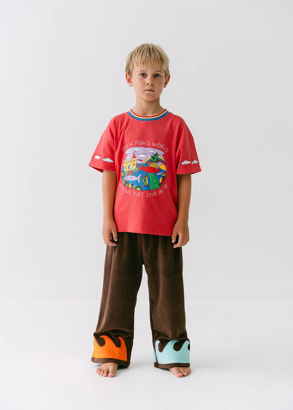 Child wearing a red t-shirt with a colorful graphic and brown pants on a white background