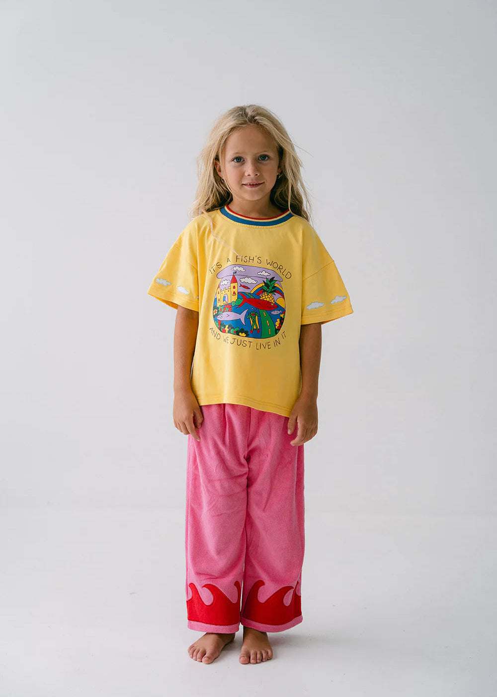 Child wearing a yellow shirt with a colorful design and pink pants on a white background