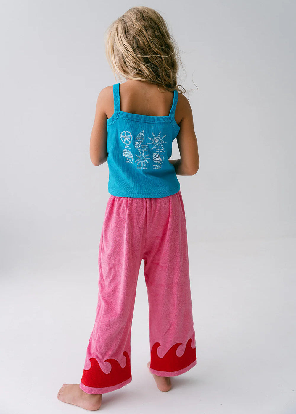 Child wearing a blue top with white designs and pink pants with red at the bottom on a plain background
