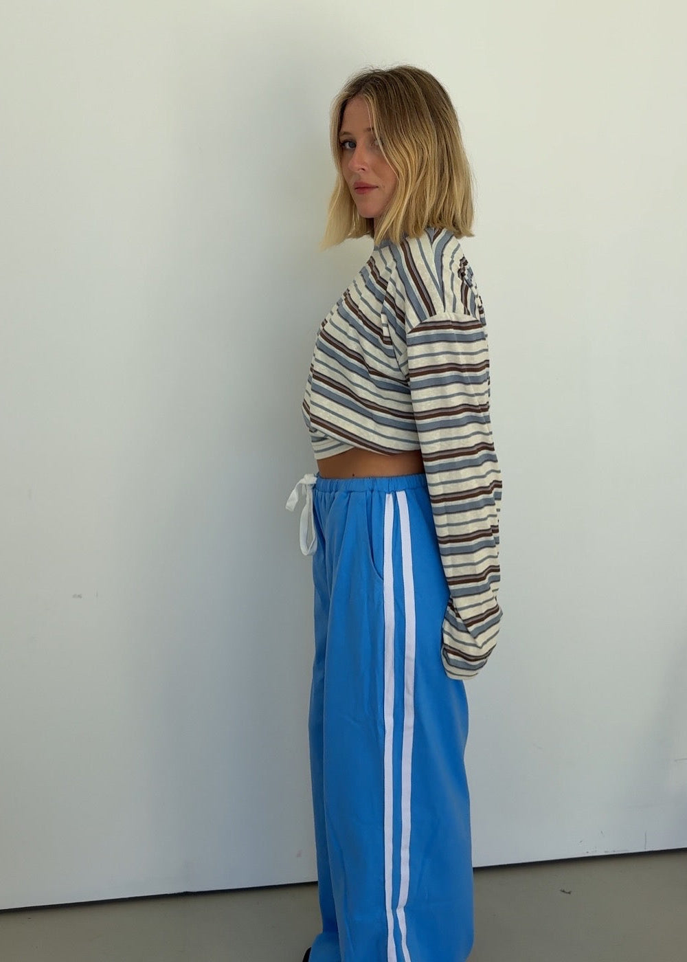Person wearing a striped sweater and blue pants with white stripes against a plain background