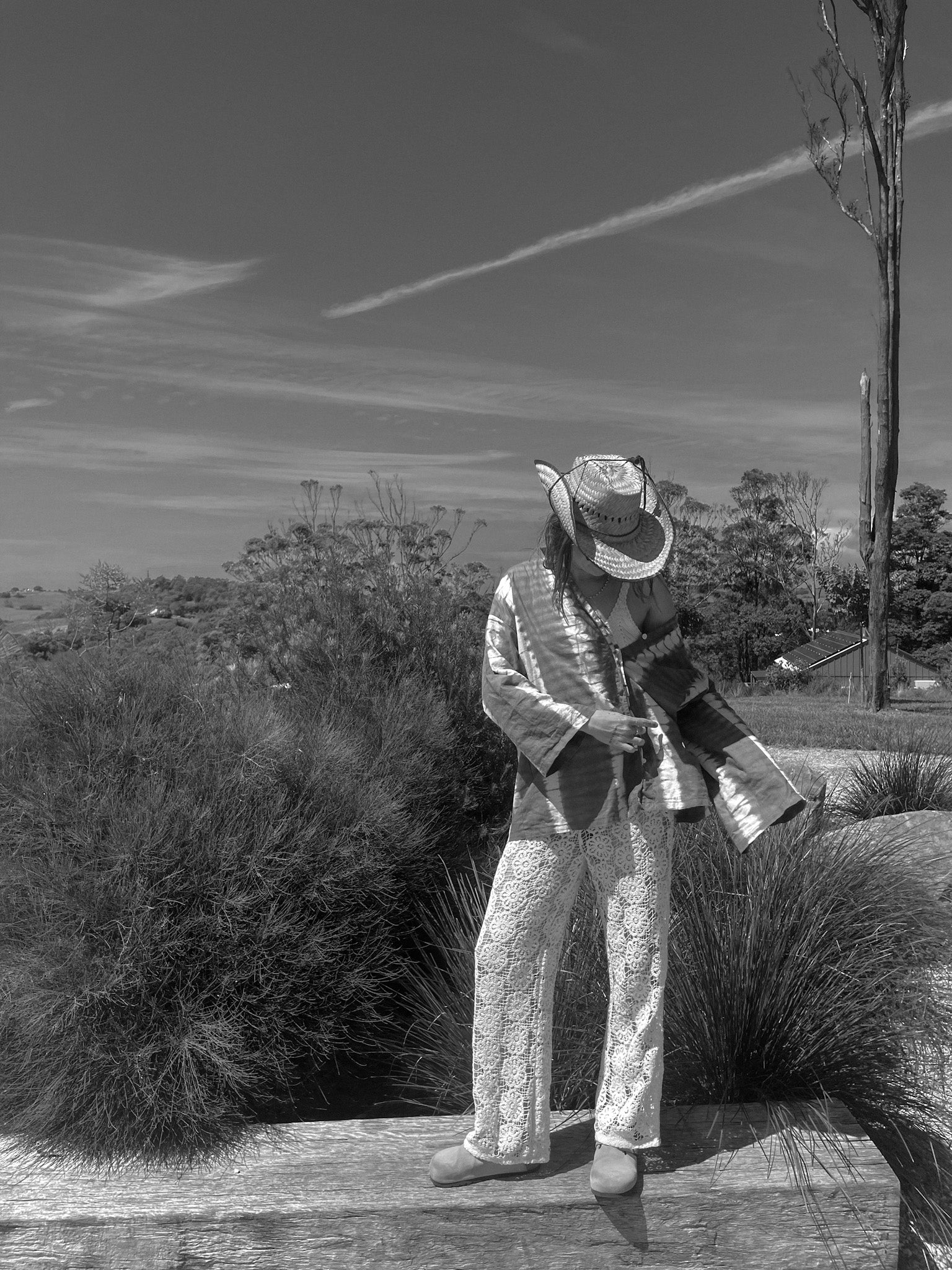Person in a patterned outfit standing outdoors with plants and sky in the background