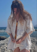 Woman in a white cover-up standing on a rocky beach with ocean in the background