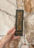 Hand holding a black box with 'Dutchie' branding against a stone wall background