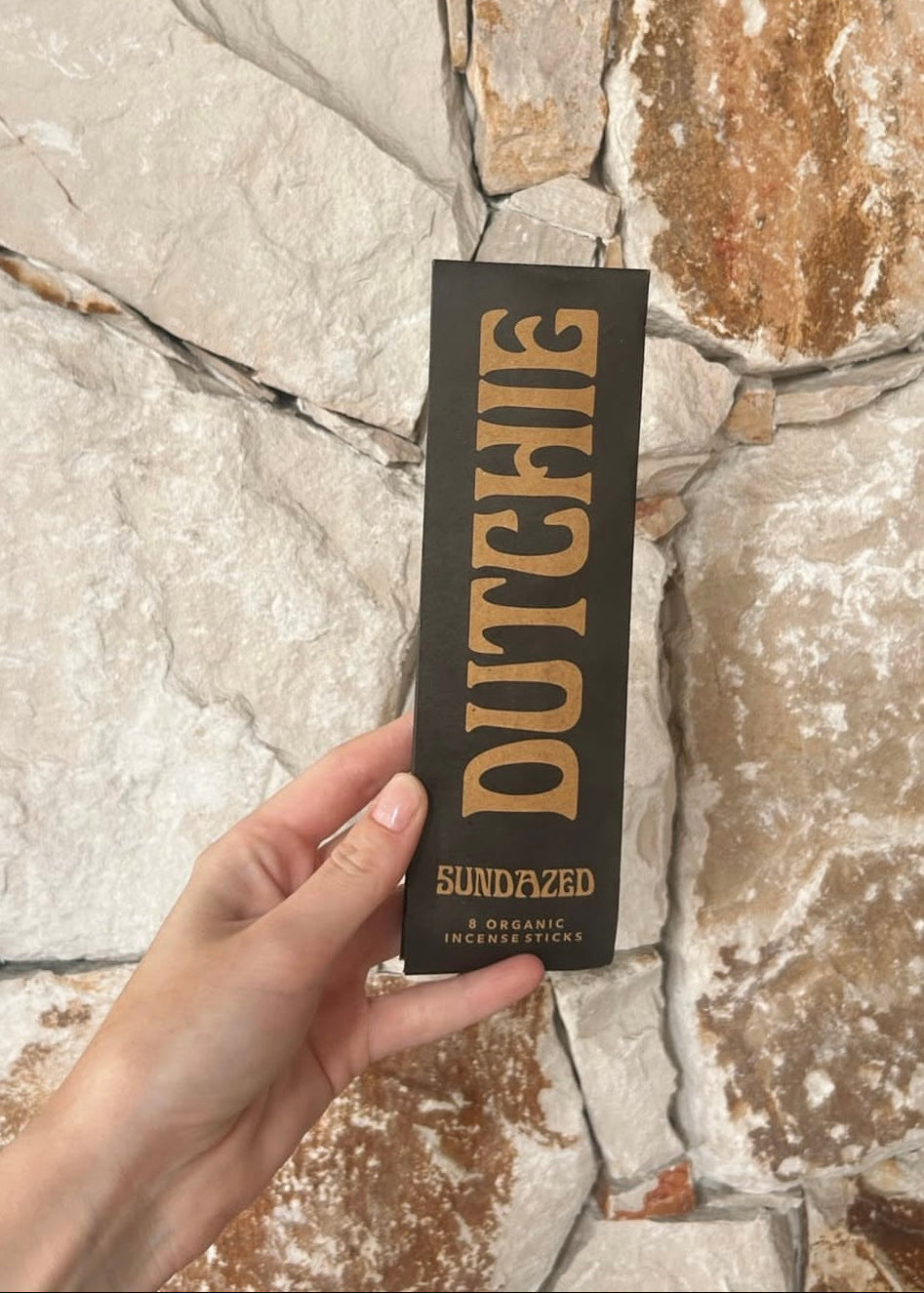 Hand holding a black box with 'Dutchie' branding against a stone wall background