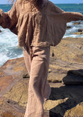 Person wearing a beige outfit standing on rocky coastal terrain with ocean waves in the background