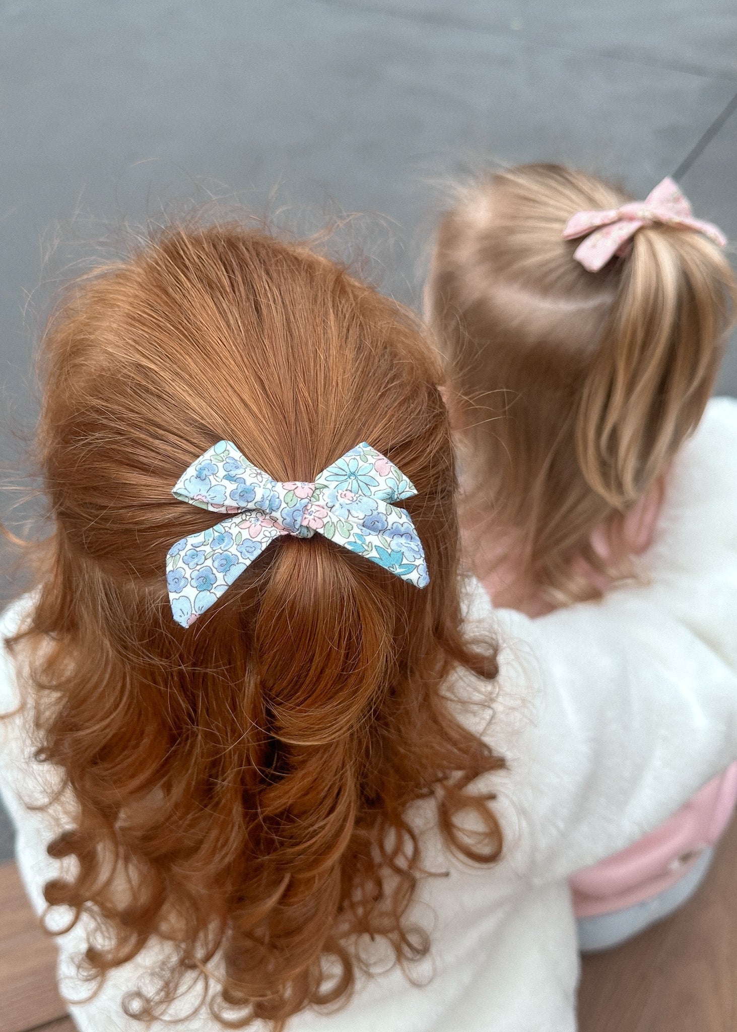 Two children with styled hair, one with a blue bow and the other with a pink bow, against a neutral background.