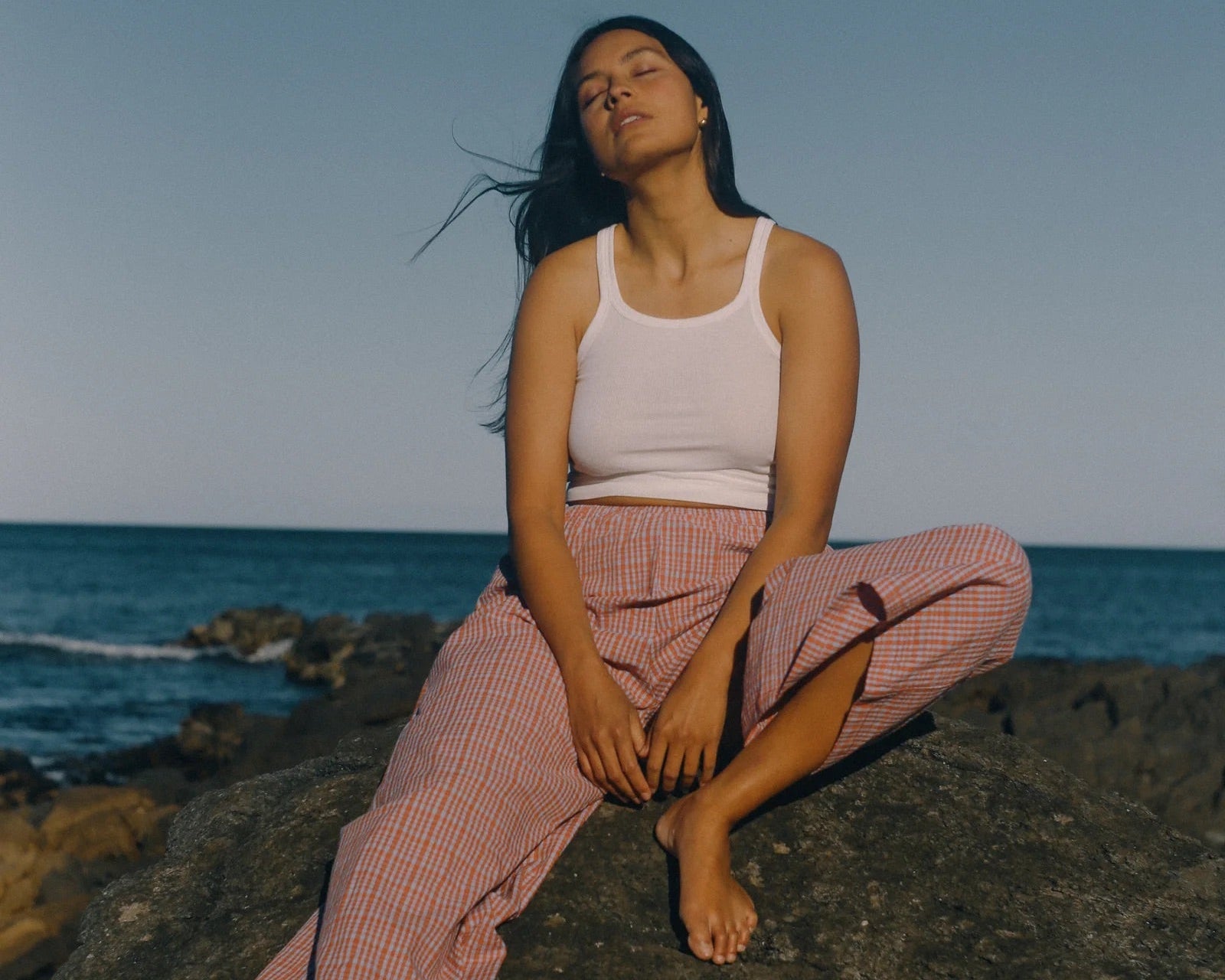 Woman sitting on a rock by the ocean with a clear blue sky.