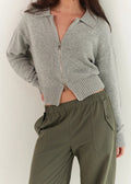 Person wearing a gray zip-up cardigan and green pants against a white background
