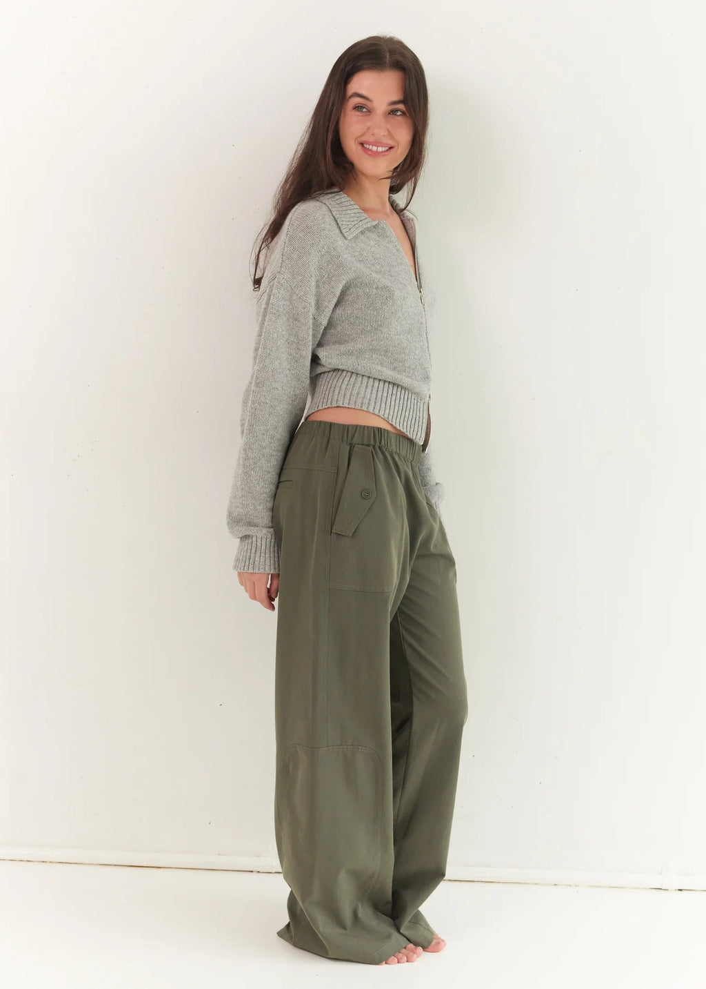 Woman wearing a gray cardigan and olive green pants against a white background