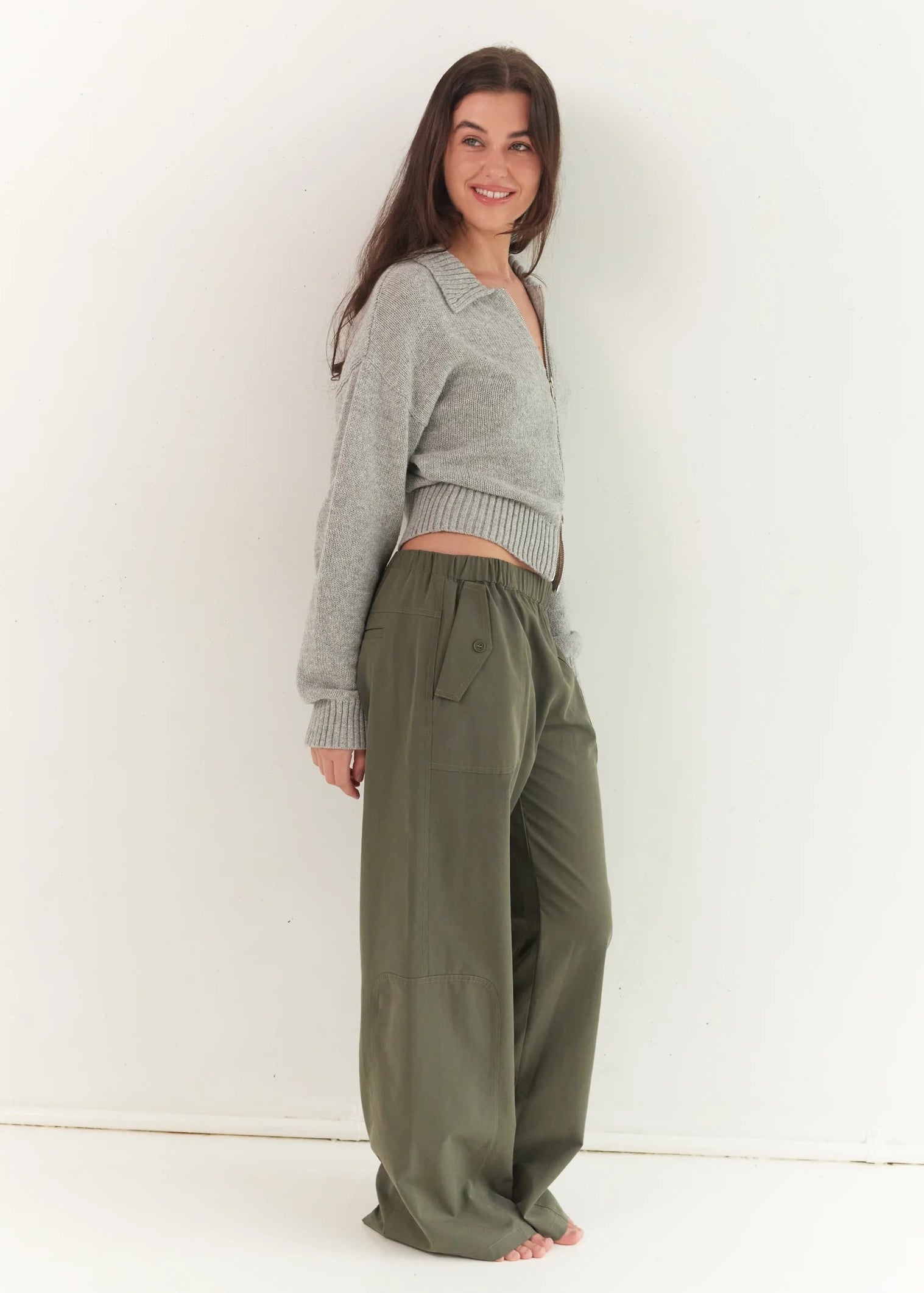 Woman wearing a gray cardigan and olive green pants against a white background