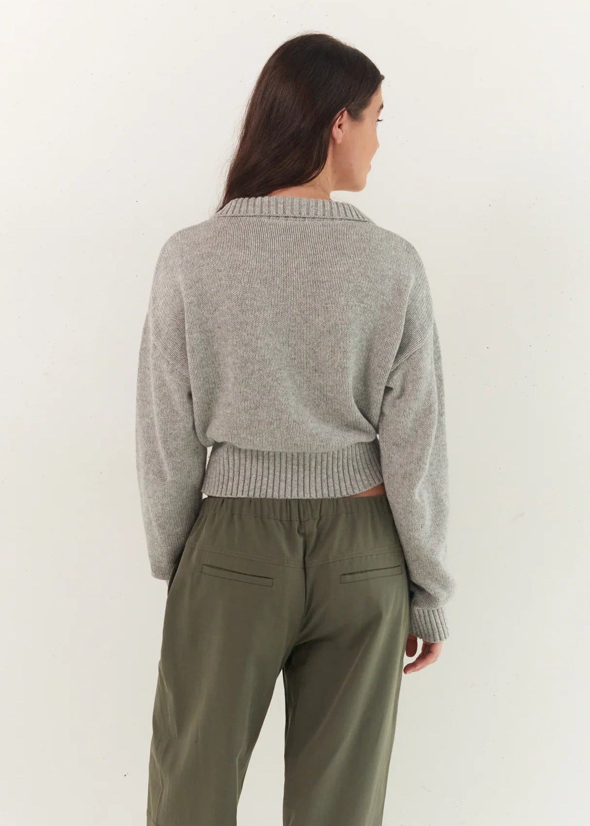 Woman wearing a gray sweater and green pants against a white background