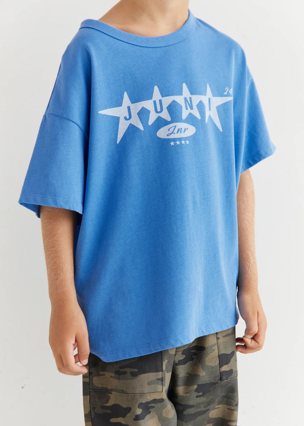 Person wearing a blue t-shirt with a graphic design and camouflage pants on a white background