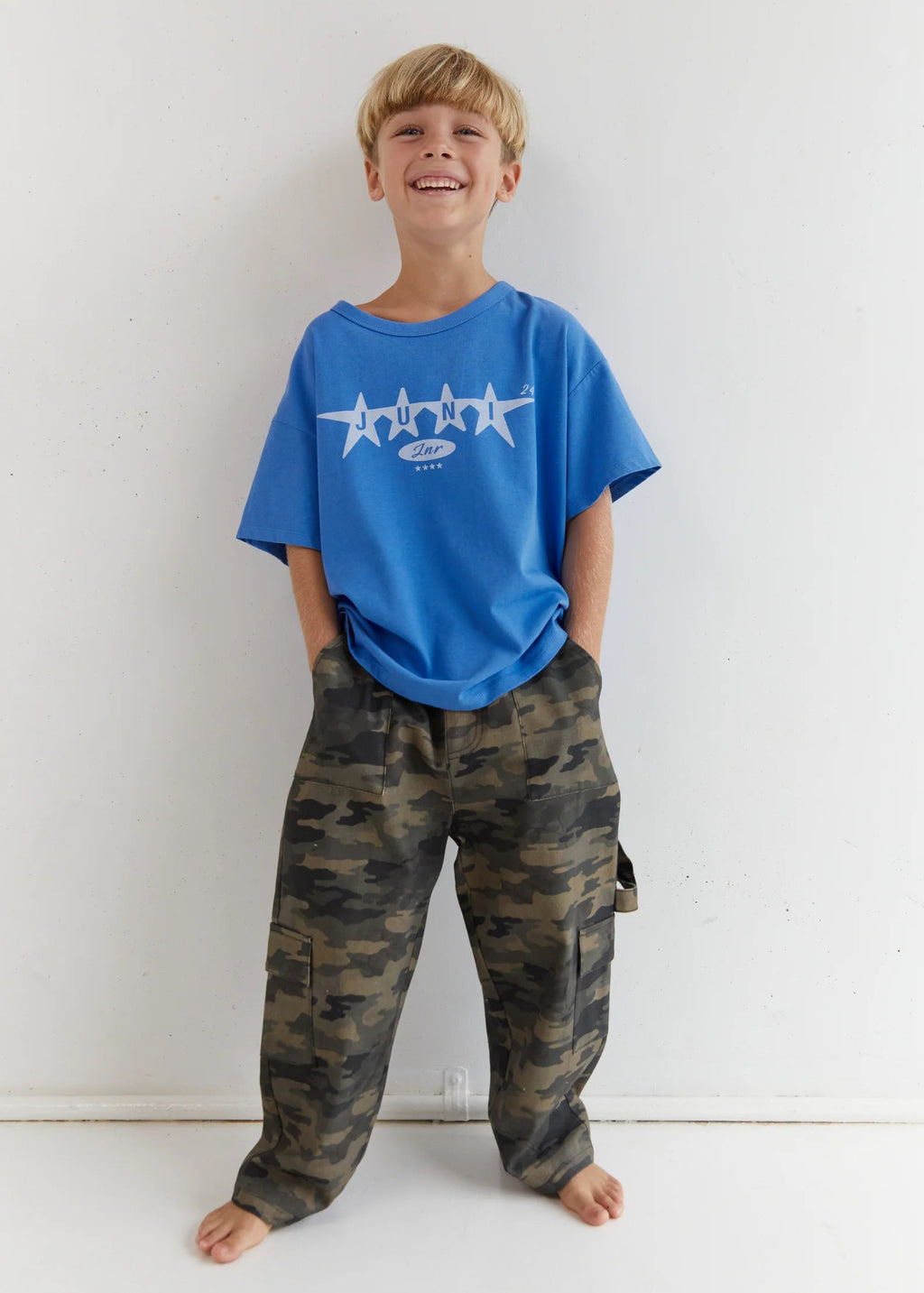 Child wearing a blue t-shirt with white stars and camouflage pants on a white background