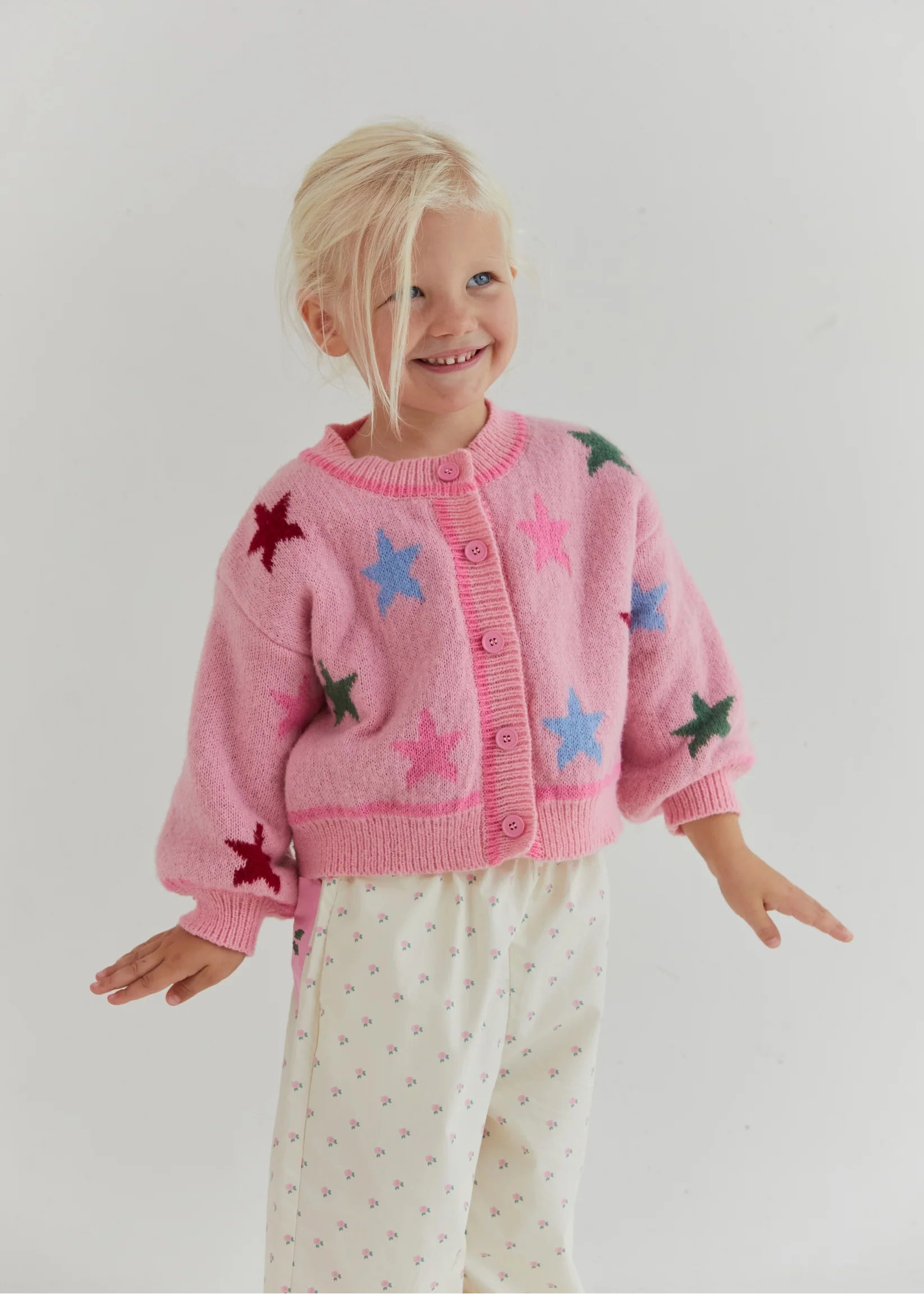 Child wearing a pink cardigan with star patterns on a plain background