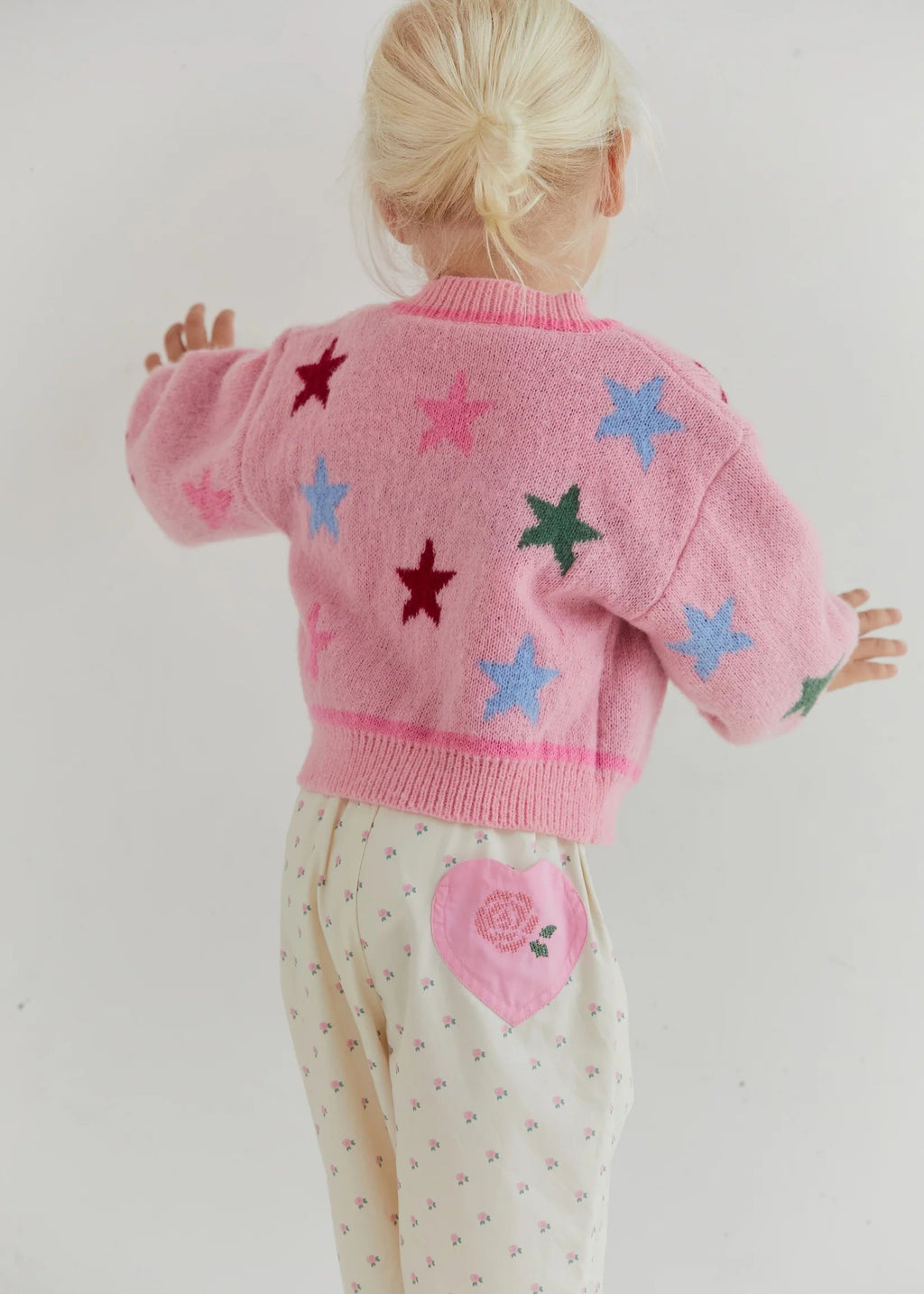 Child wearing a pink sweater with star patterns on a white background