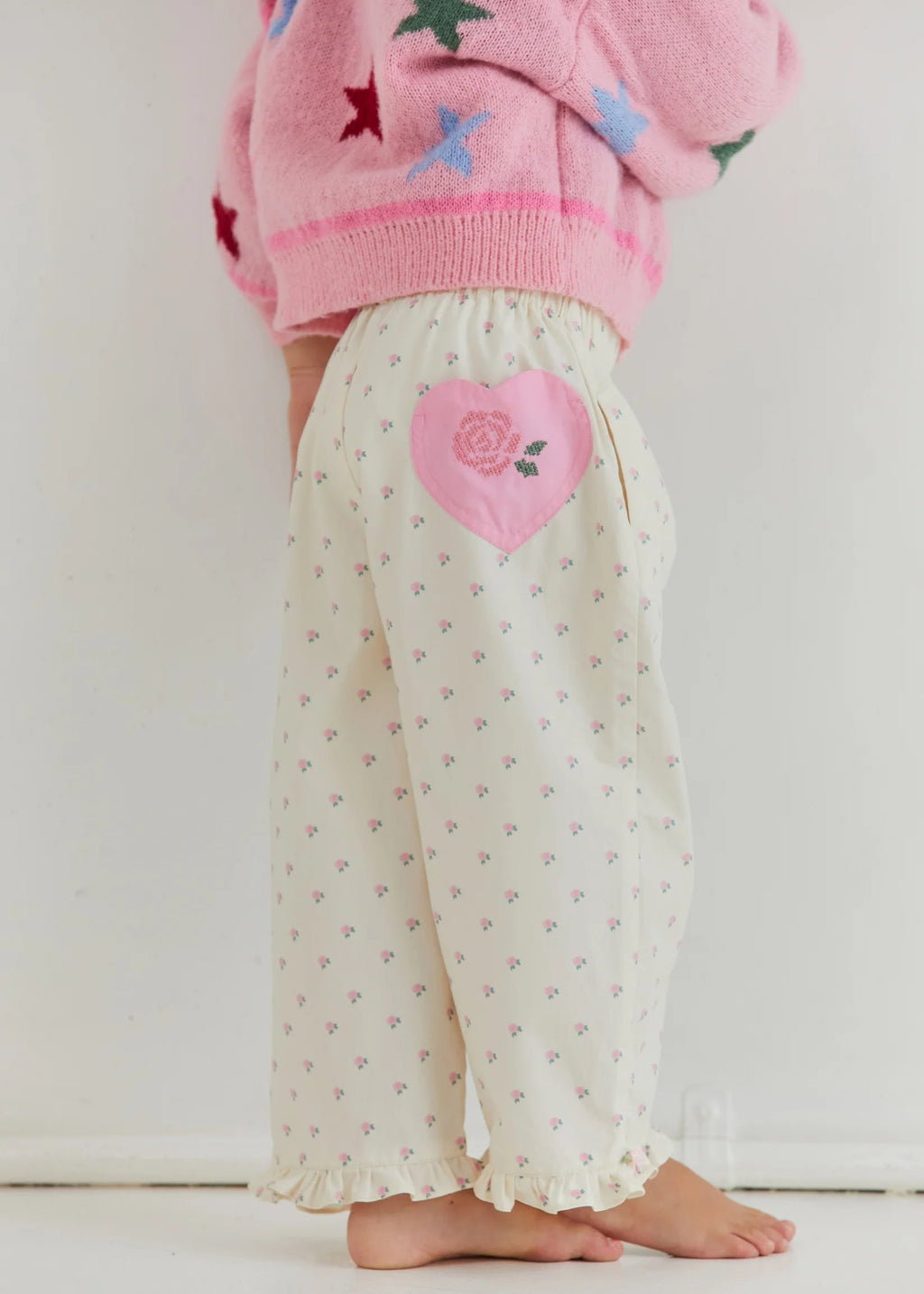 Child wearing a pink sweater with star patterns and white pants with a heart design on a white background