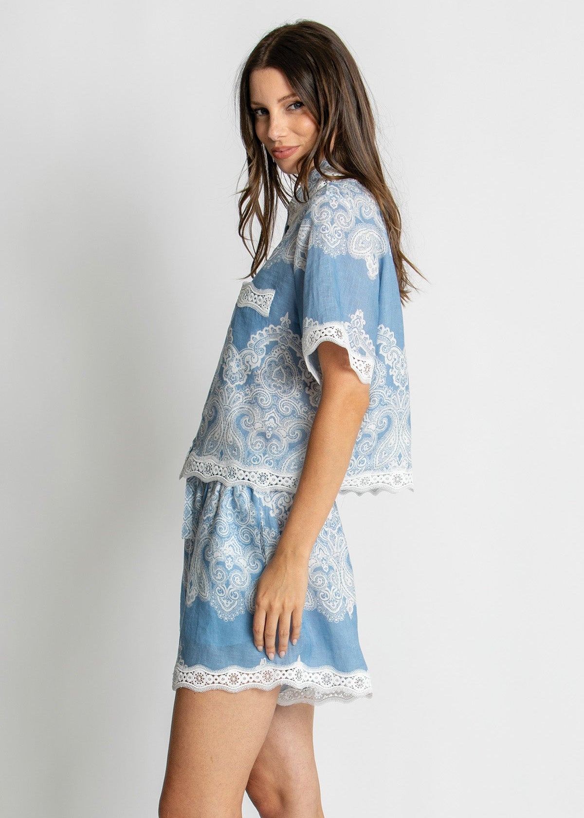 A woman modeling a light blue and white lace-trimmed short dress or cover-up with a matching skirt, photographed against a plain light gray studio background.