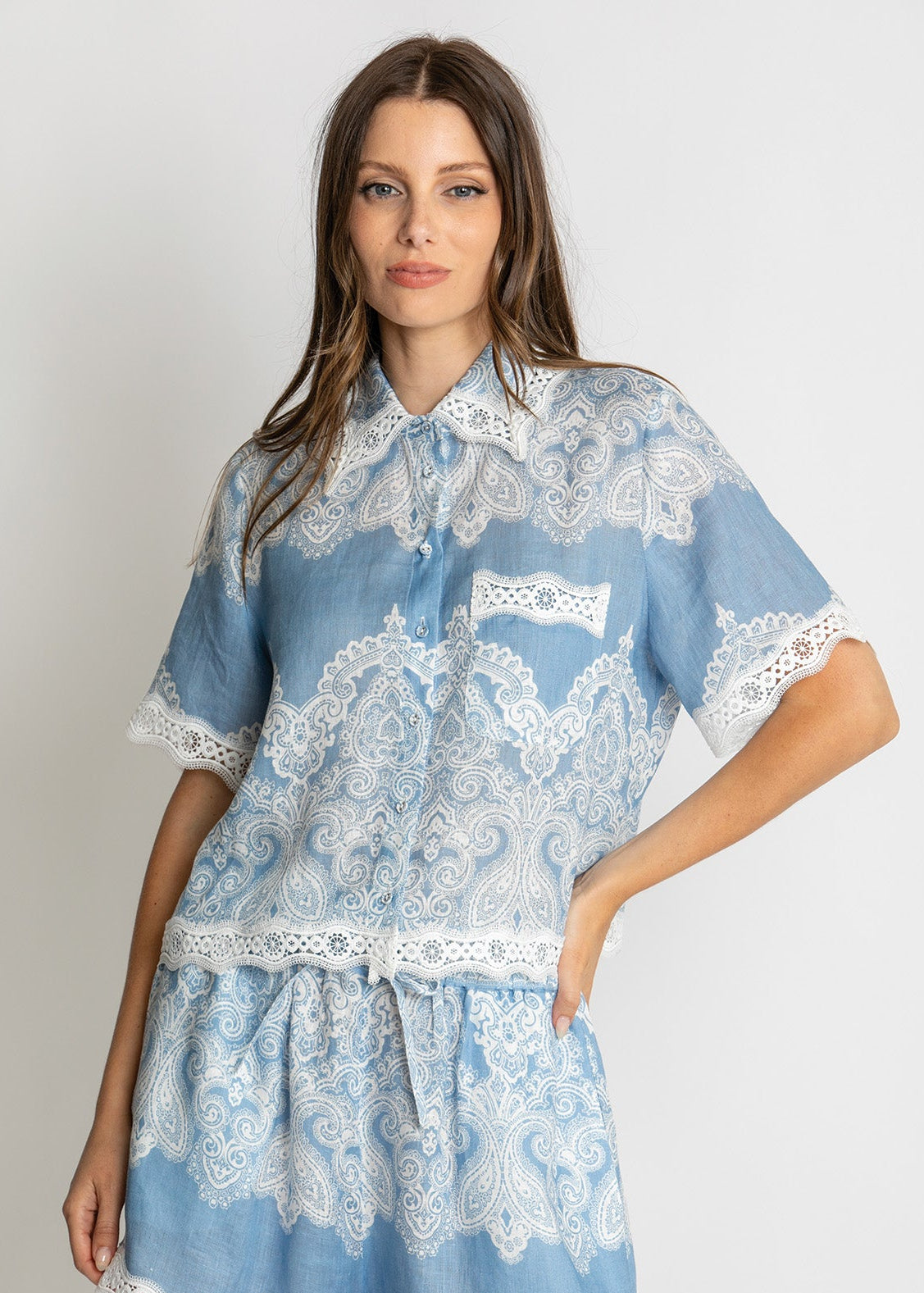 A woman modeling a light blue and white lace-patterned short-sleeve shirt and matching shorts set against a plain light gray studio background.