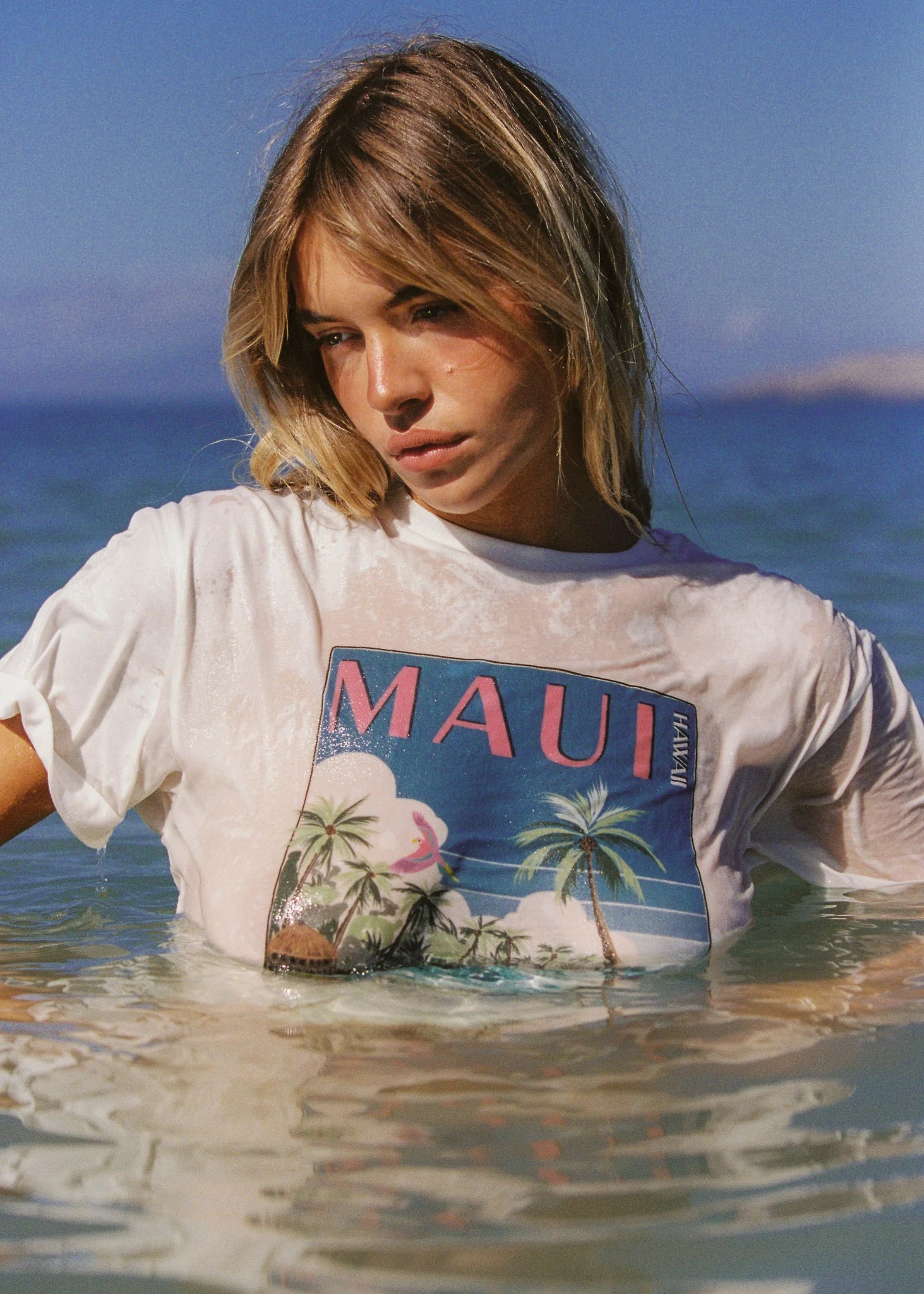 Woman wearing a 'Maui' t-shirt standing in water with a scenic background