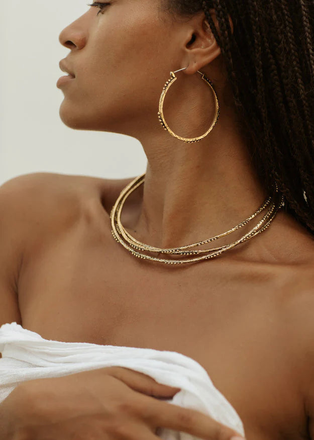 Woman wearing gold hoop earrings and necklaces against a neutral background