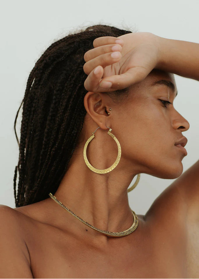 Woman wearing gold hoop earrings and a necklace against a neutral background