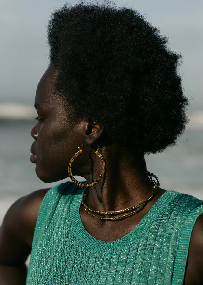 Woman with styled hair wearing gold hoop earrings and a green top against a blurred background