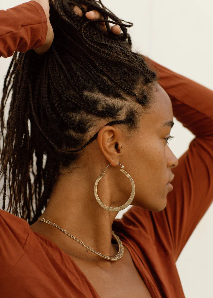 Woman with styled braids wearing a rust-colored top against a neutral background