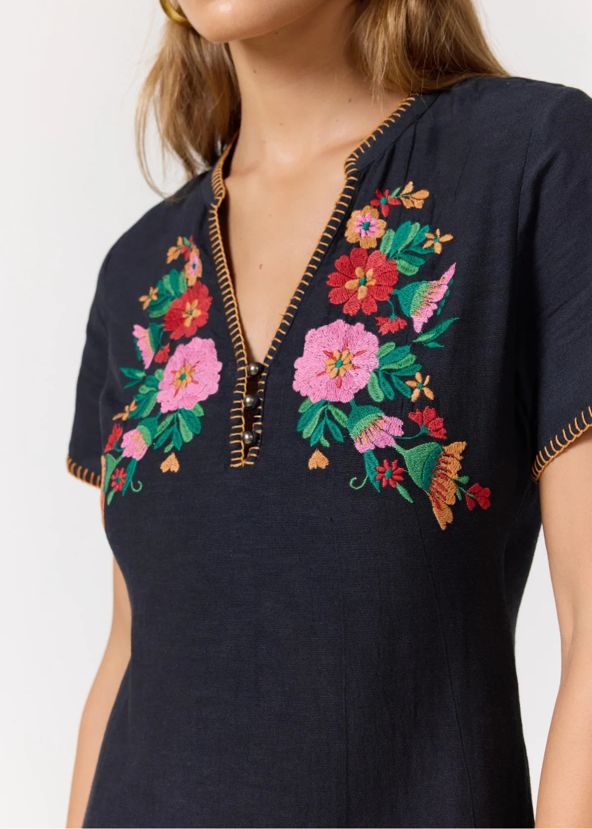 A close-up of a woman wearing a navy blue short-sleeve top with colorful floral embroidery on the chest and gold-colored zipper trim.