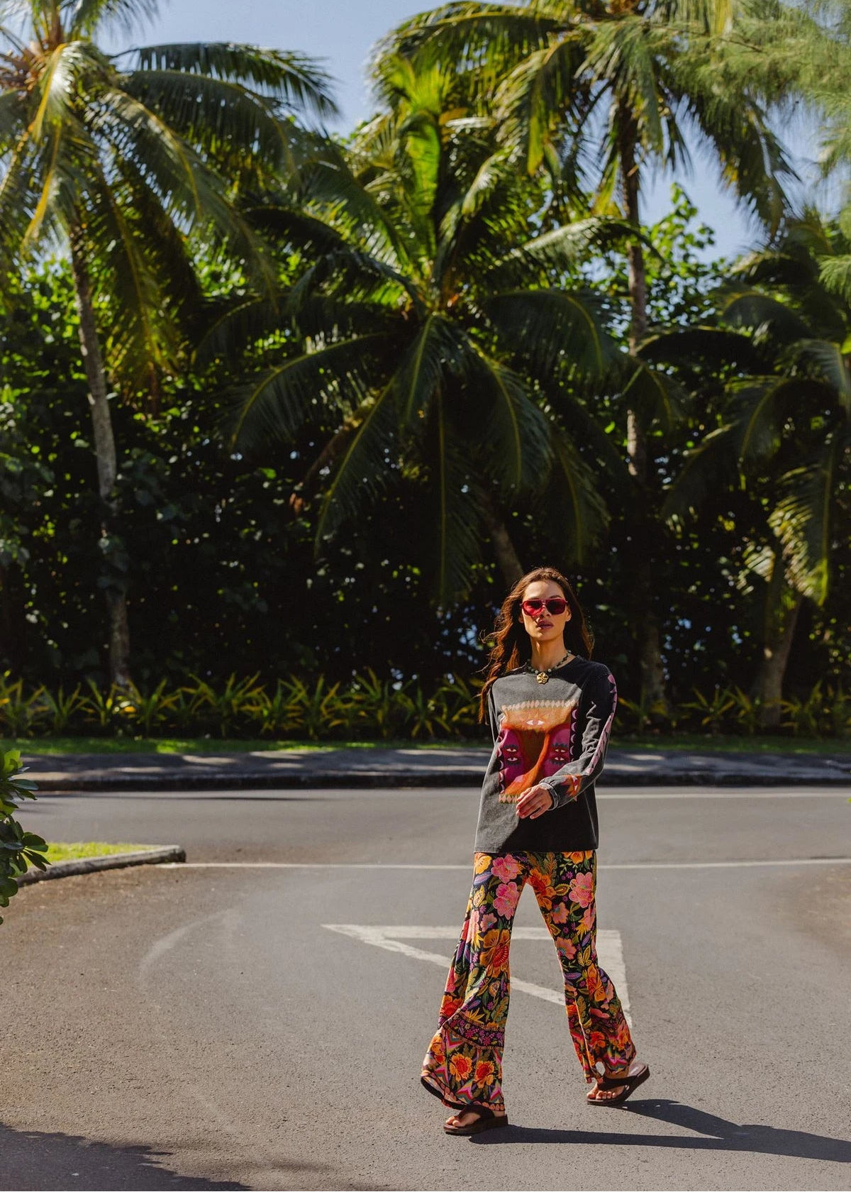 Woman in colorful outfit standing on a road with palm trees in the background