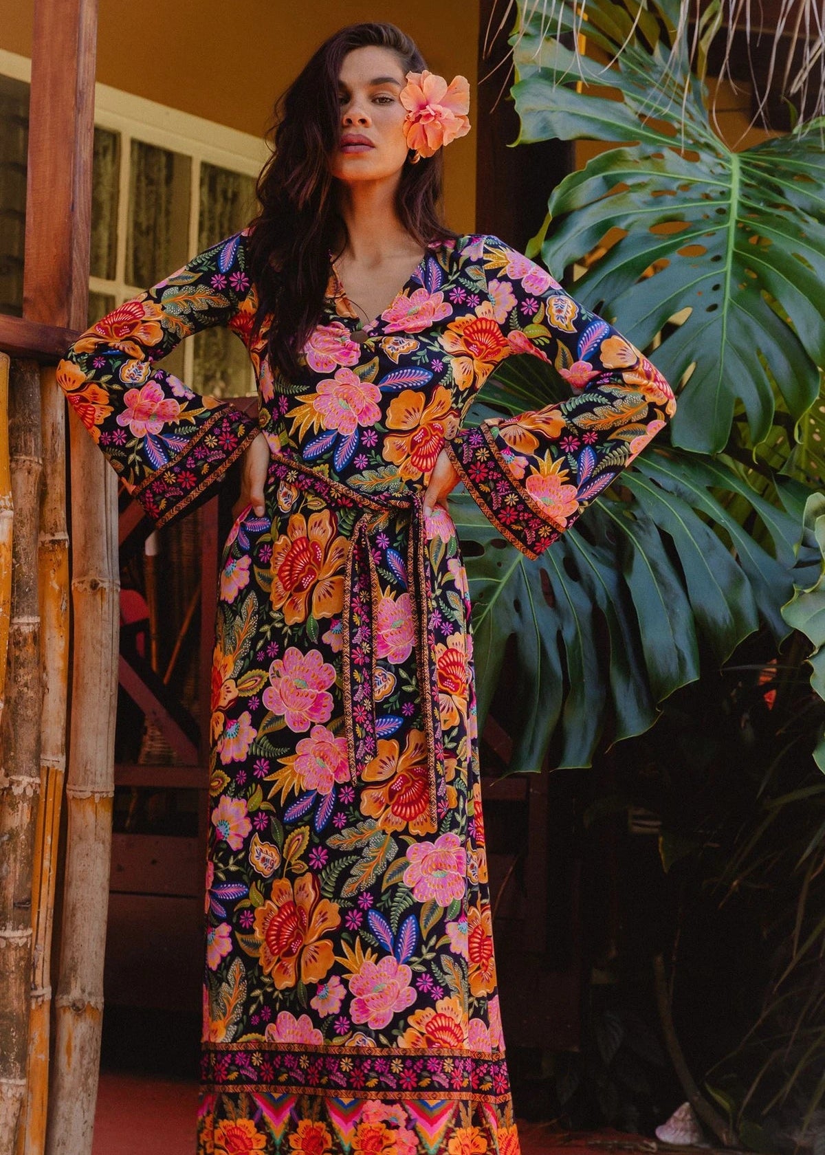 Woman wearing a colorful floral dress standing in front of green foliage.